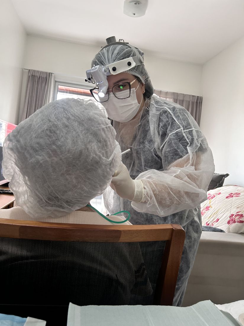 Cirurgiã-dentista da SOHD em atendimento odontológico no domicílio do paciente, com lupa e paramentação completa